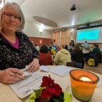 Foto von Andrea Dreffein-Hahn, die an einem Stehtisch vor der Kreismitgliederversammlung die Einlasskontrolle macht und fröhlich in die Kamera lächelt.