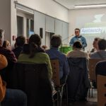 Foto eines zuhörenden Publikums auf einer Kreismitgliederversammlung. Lukas Unger steht am Redepult.