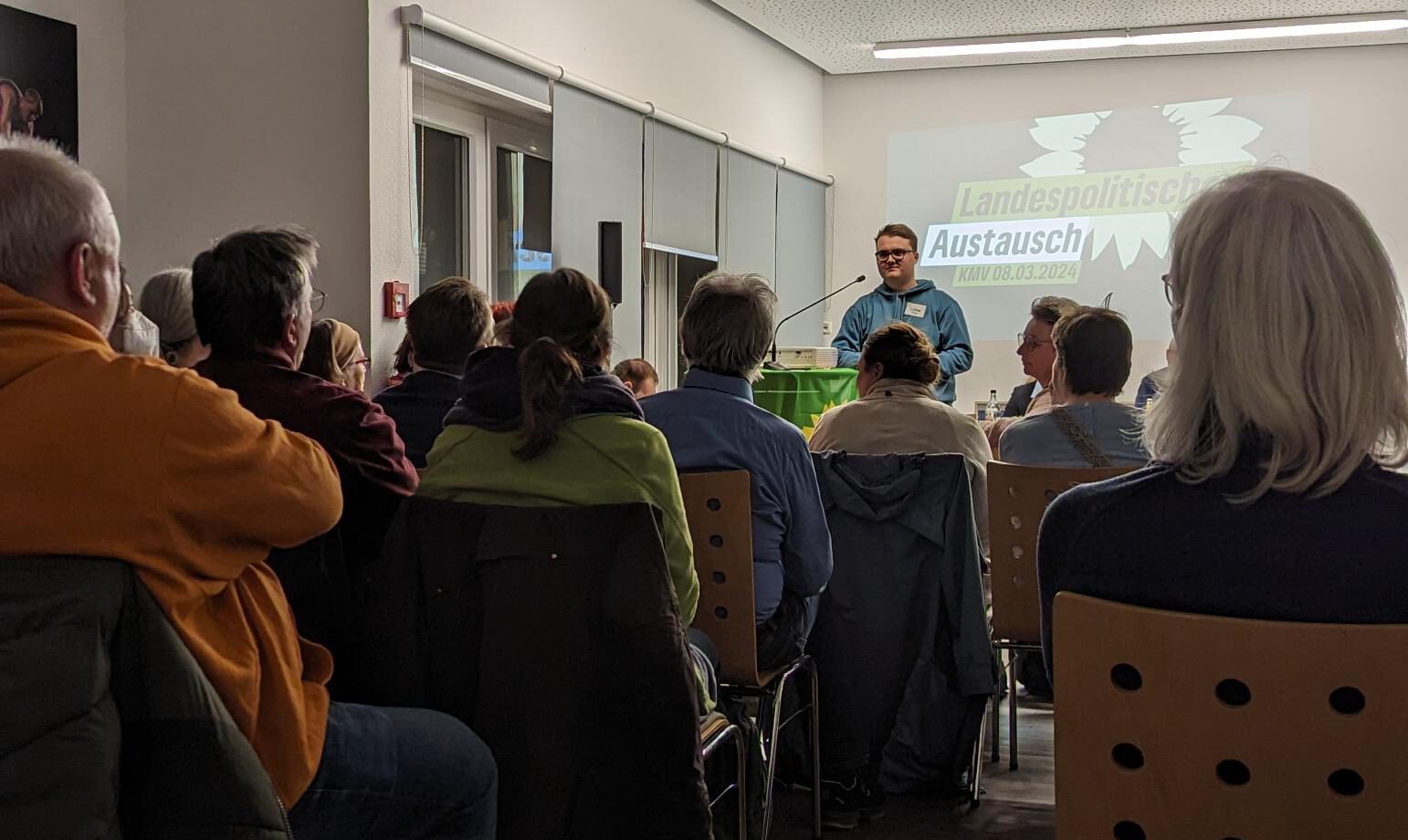 Foto eines zuhörenden Publikums auf einer Kreismitgliederversammlung. Lukas Unger steht am Redepult.