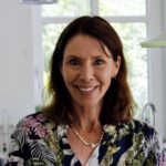 Foto von Astrid Griess, einer Frau mit heller Haut und langen braunen Haaren. Sie blickt lächelnd in die Kamera.